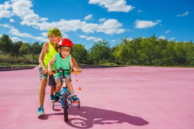 Action image of two brothers together, boy push little bicycle teaching smaller child to ride