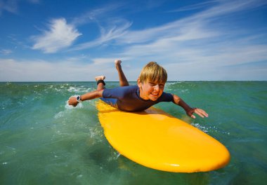 Smiling boy lay on the surf board and start to paddle to catch the wave learning at surfing school