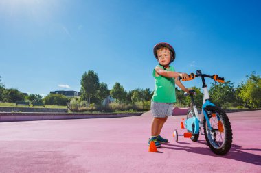 Little boy stand with his bicycle at city roller park wearing helmet and learning to ride
