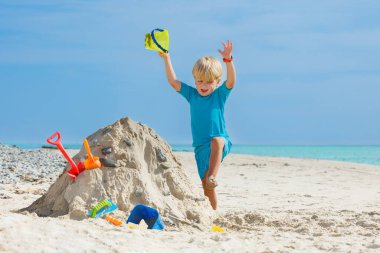 Happy smiling jumping boy play with sand shovel bucket at the ocean beach during summer vacations