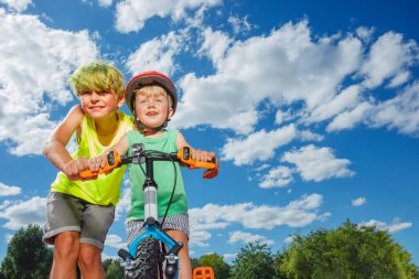 Big brother help little boy ride a small bicycle cute close-up photo of siblings posing together