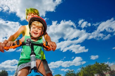 Two brother together portrait, big boy push little bicycle - fun time in the park