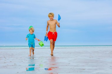 Two happy kids, boys run on an ocean beach holding buckets and hoop-net having fun catching crabs