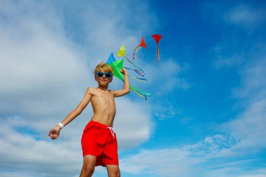 Young smiling boy close portrait stand holding many colorful kites in hand over blue sky wearing sunglasses