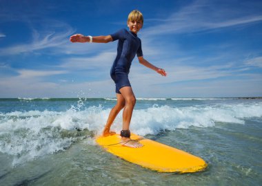 Young boy learn to stand on the surf board standing on the sea beach balancing with hands