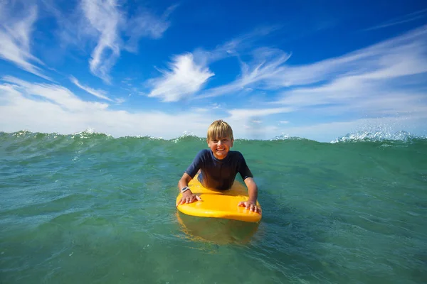 Close face portrait of smiling boy lay on the surf board looking at camera in the sea starting to ride the wave