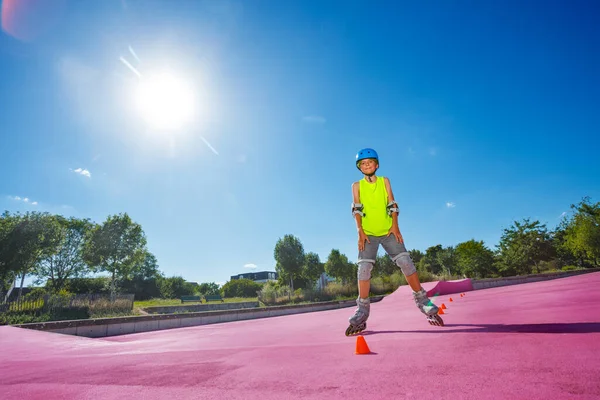 Teen boy pose standing in blue helmet on rollerblades in the skatepark wearing protection and going around cones