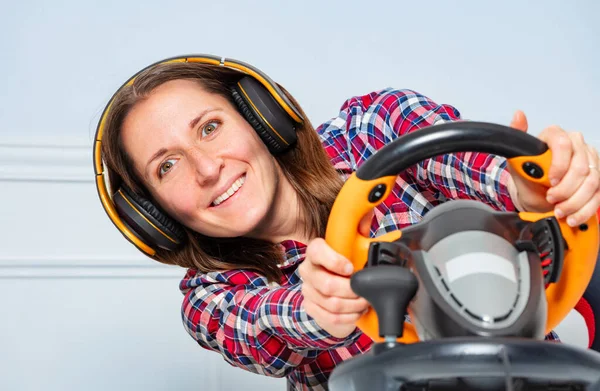 Happy engaged and laughing gamer woman with hands on steering wheel in headphones playing race game