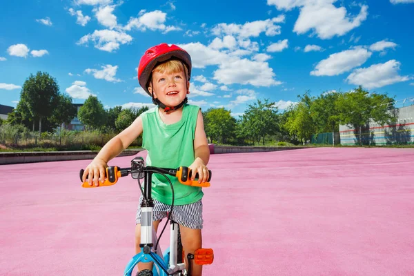 Little blond smiling boy ride small bicycle on color surface of the park
