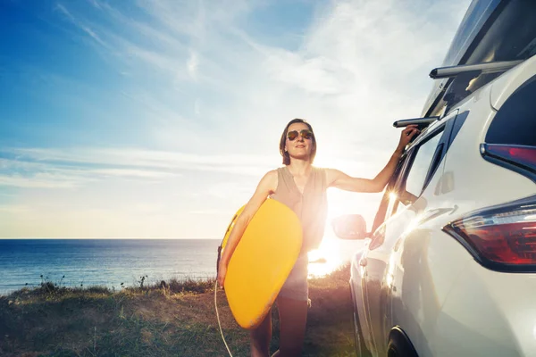 戴着太阳镜的女人站在汽车旁边 从后面俯瞰大海的日落 — 图库照片