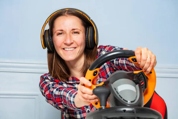 Happy smiling and laughing gamer woman with hands on steering wheel in headphones playing race game