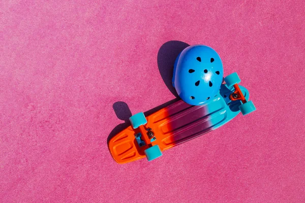 Skateboard and helmet view from above on the color pink surface of a skatepark