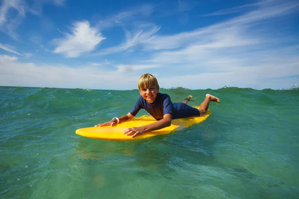 Portrait of smiling boy lay on the surf board looking at camera in the sea starting to ride the wave