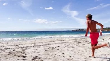 Happy little boy running in ocean at the sand beach on the summer vacation