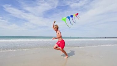 Çocuk renkli bir uçurtmayla deniz ve kumsalda koşuyor. Hareket dinamik konsepti.