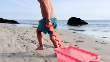 Happy little Caucasian blond boy run with toy  on beach over ocean waves