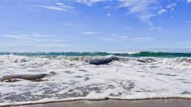 Sea waves surf on the beach during summer day with splashes 
