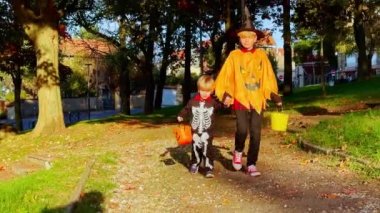 Cadılar Bayramı 'nda kılık değiştirmiş iki kardeş parkta şeker kovası tutuyor.