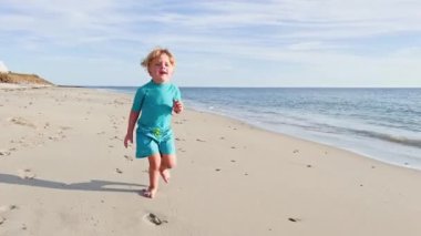 Happy little blond boy running  on the sand beach