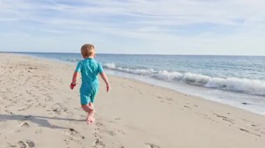 Happy little blond boy running  on the sand beach
