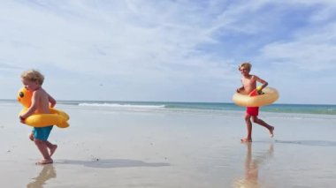 Two happy kids boys with inflatable toy buoys  having fun running on the sand beach