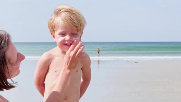 楽しいですオンザビーチお母さんApply Tan日焼け止めUvクリーム運ぶのために少しかわいいですブロンド男の子で夏休み — ストック動画