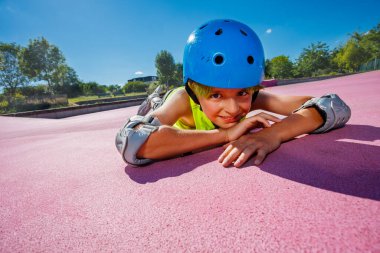 Young boy in blue helmet and rollerblades in the skatepark rest on the color surface smiling