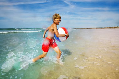 Young boy in orange sunglasses in sea with inflatable ball view from side