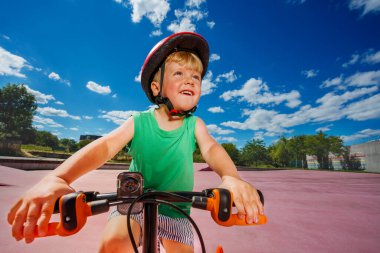 W low angle portrait of a little blond smiling boy ride small bicycle on color surface of the park