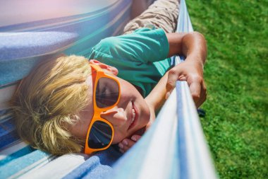 Happy smiling young boy in orange sunglasses lay in hammock close portrait turning head up and smile