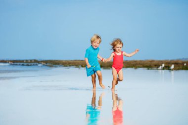Cute little boy and girl run on sand beach over ocean waves holding hands smiling having fun