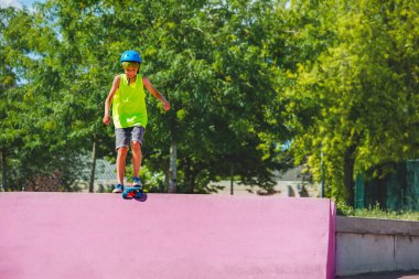 Preteen boy in skate park stand on top of the color ramp wearing helmet