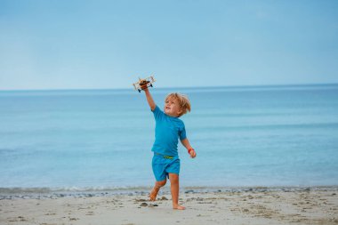 Little boy run with toy model of the plane over calm ocean and beach on background
