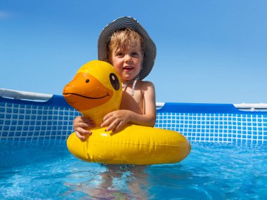 Little boy in the pool stand in inflatable duck playing in the water and smiling