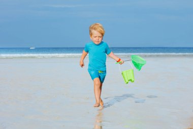 Little blond boy run from ocean holding buckets and hoop-net having fun, play on a beach at summer
