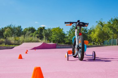 Little children learning bicycle with extra wheels at the city skate park