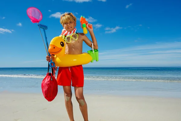 Fun relax vacation boy with many toys inflatable duck, butterfly net scuba stand on the sea beach