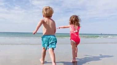Two happy little kids  run on the sand beach in ocean waves on summer vacation 