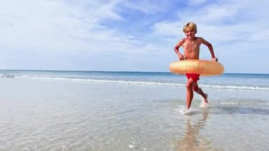 Happy handsome boy with inflatable doughnut buoy run smiling on the sand beach