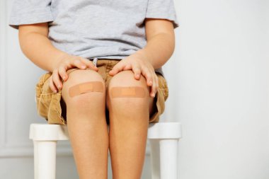 Elleri ve parmakları dizlerinin üzerinde yatarken, bir yara bandı ile genç bir çocuğun dizinin detaylı görüntüsü