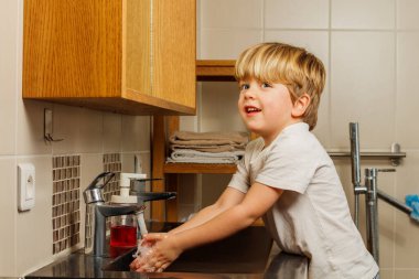 Mutlu yakışıklı çocuk onları suyun altında tutarak banyoda ellerini yıkıyor.