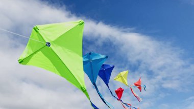 Group of many beautiful colorful kites fly on the string over blue sky with clouds