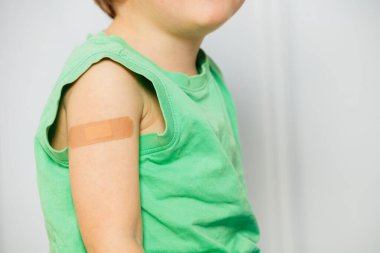 Yeşil gömlekli, omzunda yara bandı olan yakışıklı bir çocuğun yakın çekimi.