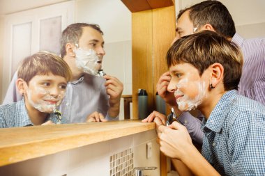 Baba ve oğul yakın plan çekimleri. Banyoda birlikte tıraş olurken aynaya bakıp tişört giyerek eğleniyorlar.