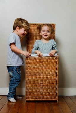 İki mutlu küçük çocuk, ahşap çamaşır kutusunda saklanarak oyun oynuyor. Kız ve oğlan evde eğleniyorlar.