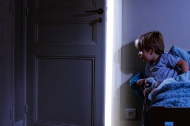 Yatak odasındaki sevimli çocuk, açık kapıdan gelen ışığa bak.