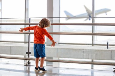 Küçük çocuk havaalanının penceresinin yanında durup uçağa bakıyor. Dışarı çıkıyor, el sallıyor ve uçuyormuş gibi yapıyor.