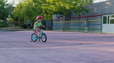 Küçük mutlu çocuk kaykay parkında direksiyon ve pedallarla bisiklet sürmeyi öğreniyor.