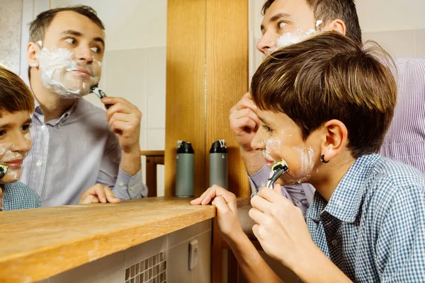 Dad teaching teen son shaving first shave experience in front of bathroom mirror