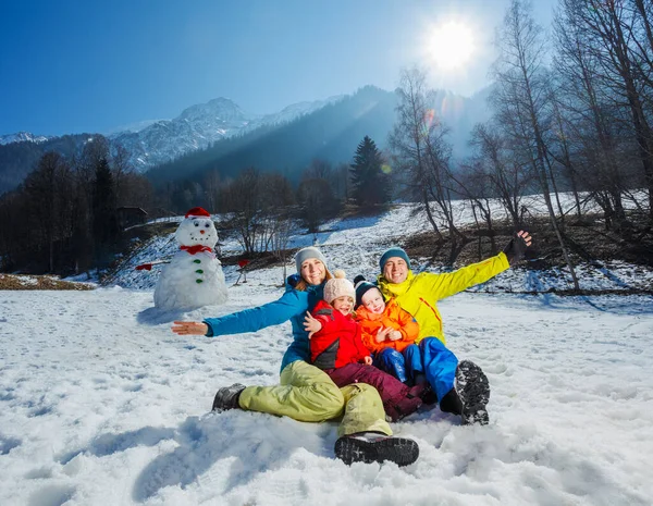 有两个孩子的家庭 妈妈爸爸在雪地里玩得很开心 他举起双手坐在雪人和高山上 — 图库照片